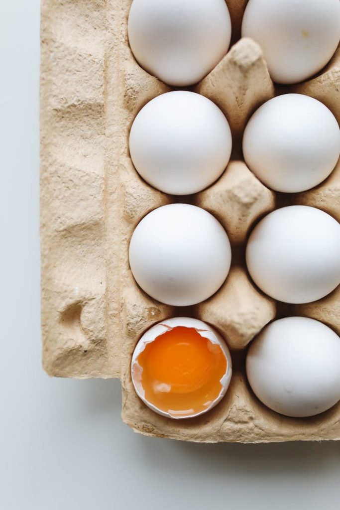 A carton of white eggs with one cracked, revealing vibrant yolk. Ideal for food and health themes.